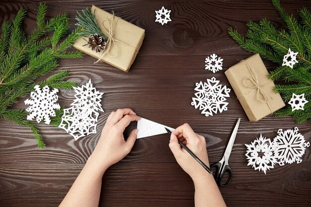 Mãos fazendo flocos de neve de papel branco na mesa de madeira