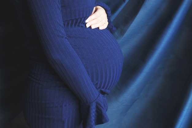 Mãos fechadas da barriga da mulher grávida abraçando a barriga em fundo azul conceito de saúde materna