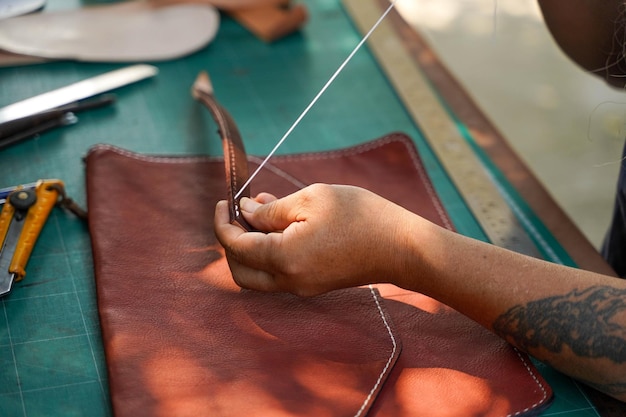 Mãos fechadas e cortadas do artesão de couro costurando uma bolsa marrom de couro para um cliente