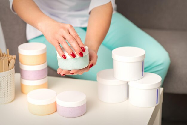 Mãos femininas abrem um frasco de creme corporal branco sobre a mesa com muitos frascos de cosméticos.