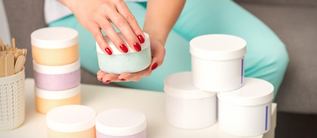 Mãos femininas abrem um frasco de creme corporal branco sobre a mesa com muitos frascos de cosméticos.