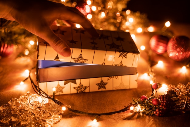 Mãos femininas, abrindo a caixa de presente de Natal acima da mesa de madeira.