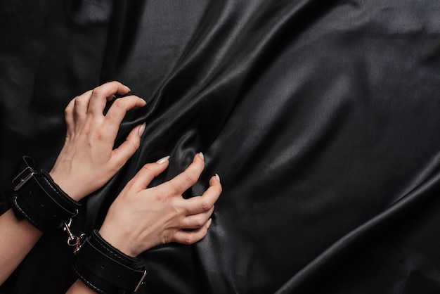 Mãos femininas algemadas em um lençol de seda escuro