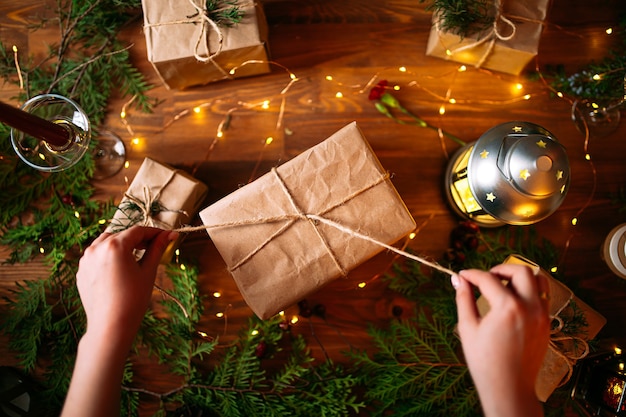 mãos femininas amarrando uma caixa de presente de artesanato de Natal com galhos de abeto na mesa de madeira