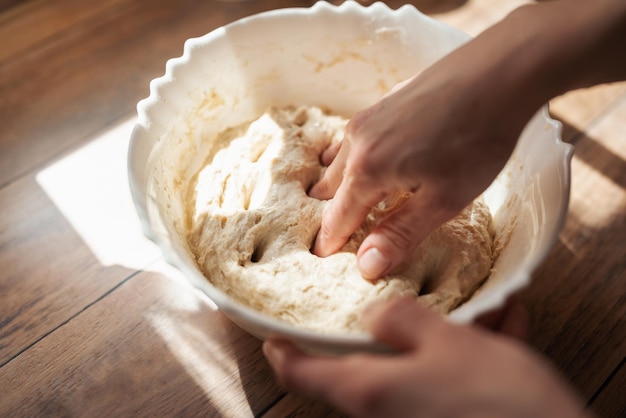 Mãos femininas amassando massa na tigela vista superior do processo de preparação de pão de centeio caseiro