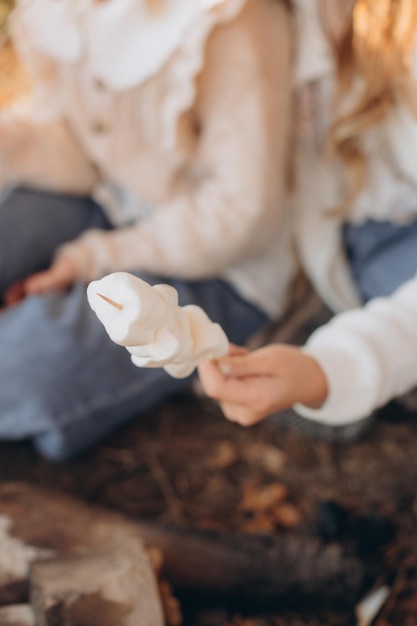 Mãos femininas assam o marshmallow amarrado em paus sobre uma fogueira aberta closeup