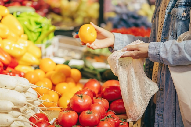 Mãos femininas colocam frutas e legumes em uma sacola de produtos de algodão no mercado de alimentos. Saco ecológico reutilizável para fazer compras. Estilo de vida sustentável. Conceito ecológico.