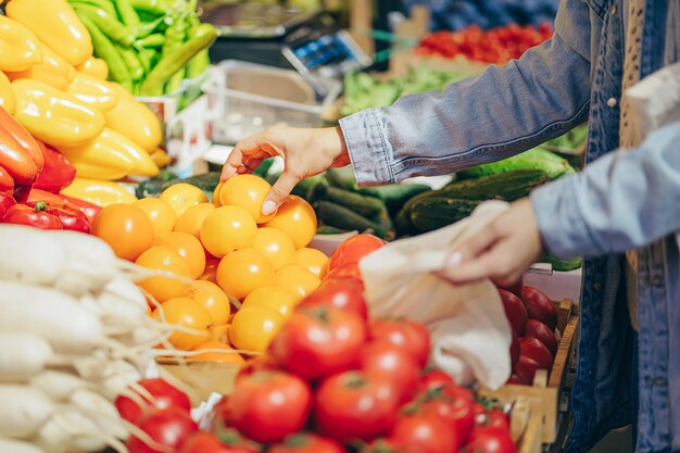 Mãos femininas colocam frutas e legumes em uma sacola de produtos de algodão no mercado de alimentos. Saco ecológico reutilizável para fazer compras. Estilo de vida sustentável. Conceito ecológico.