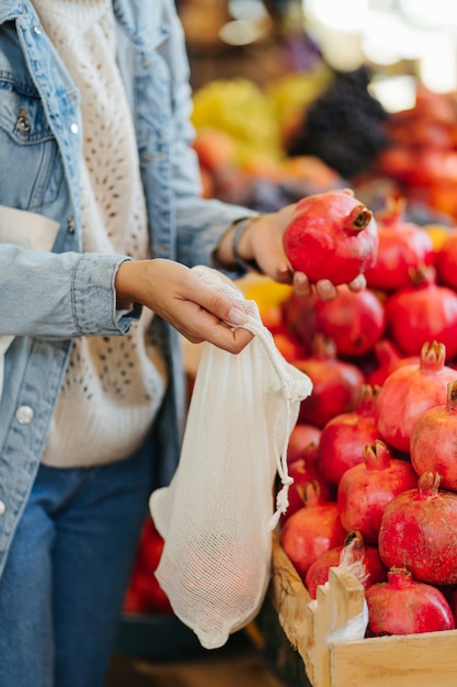 Mãos femininas colocam frutas e legumes em uma sacola de produtos de algodão no mercado de alimentos. Saco ecológico reutilizável para fazer compras. Estilo de vida sustentável. Conceito ecológico.