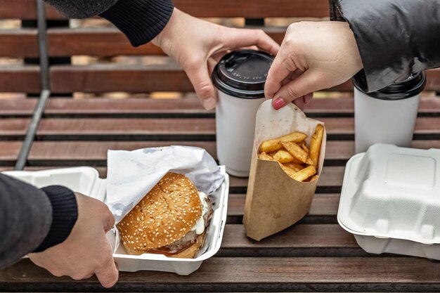 Foto mãos femininas colocam hambúrgueres com xícaras de café frito em um banco de parque comida rápida para levar