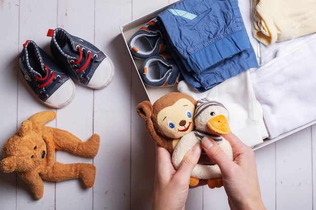 Mãos femininas colocam roupas infantis, sapatos e brinquedos em uma caixa Conceito de reciclagem de roupas de segunda mão
