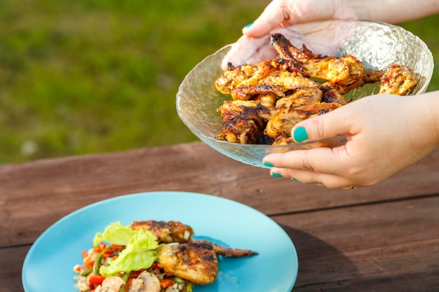 Mãos femininas colocam um prato com frango e legumes na mesa ao lado de um prato com frango grelhado