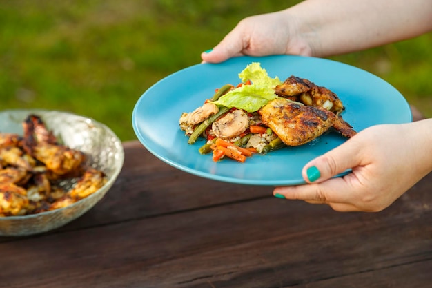 Mãos femininas colocam um prato com frango e legumes na mesa ao lado de um prato com frango grelhado