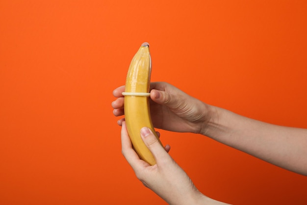 Mãos femininas colocando um preservativo em uma banana em um fundo laranja