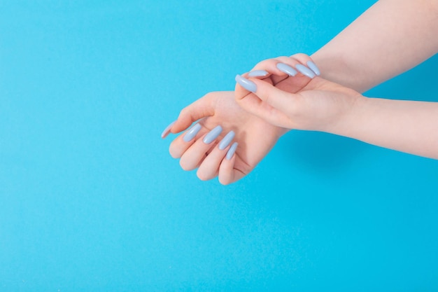 Mãos femininas com bela manicure azul sobre fundo azul