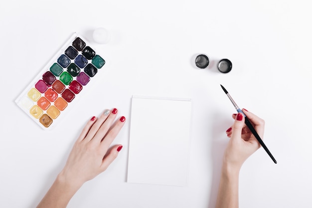 Mãos femininas com esmalte vermelho pintaram aquarelas em um notebook