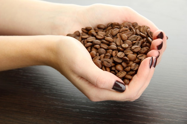 mãos femininas com grãos de café em fundo de madeira