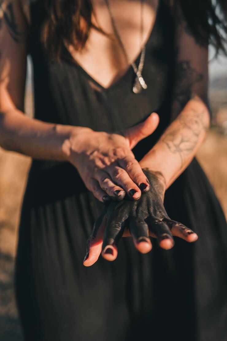 Foto mãos femininas com lama escura esfregada sobre elas e unhas pretas para mostrar conexão com a terra