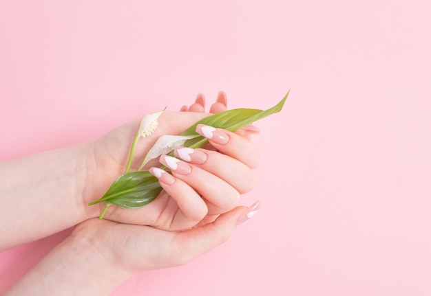 Mãos femininas com lindas unhas compridas com flores no fundo rosa