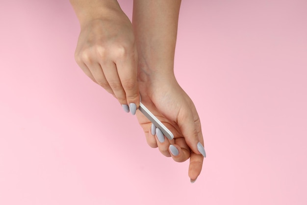 Mãos femininas com lixa de unha em fundo rosa
