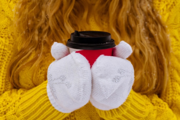 Mãos femininas com luvas segurando um copo de papel descartável com café, close-up