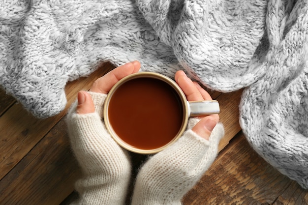 Mãos femininas com luvas segurando uma xícara de café, closeup