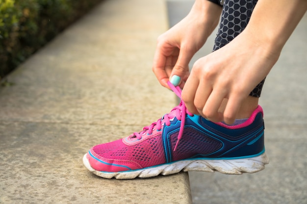 Mãos femininas com manicure amarrar cadarços em tênis rosa e azuis enquanto jogging no parque