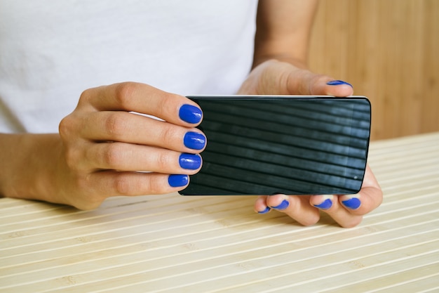 Mãos femininas com manicure azul segurando smartphone