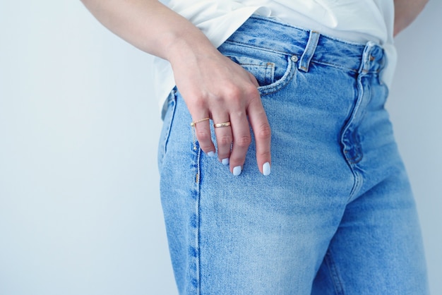 Mãos femininas com manicure perfeita em calças jeans e camiseta básica branca