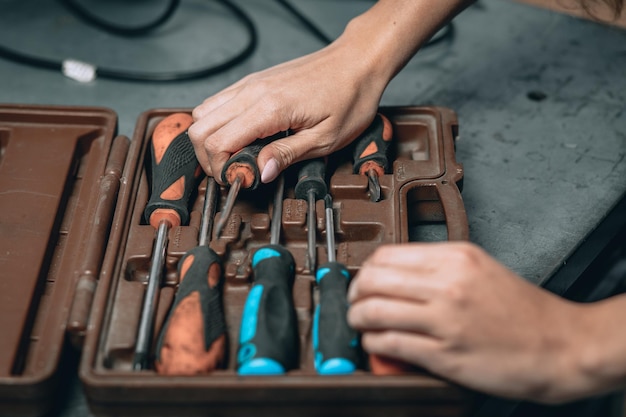 Mãos femininas com manicure rosa e caixa marrom com chaves de fenda na garagem