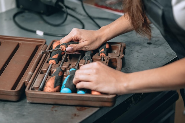 Mãos femininas com manicure rosa e caixa marrom com chaves de fenda na garagem