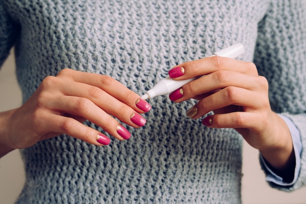 Mãos femininas com manicure rosa segurando o produto cosmético