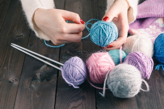 Mãos femininas com manicure roxo são raios de malha de metal de uma mesa de madeira.