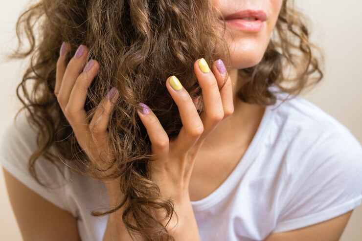 Mãos femininas com uma manicure roxa e amarela brilhante, segurando o cabelo castanho encaracolado
