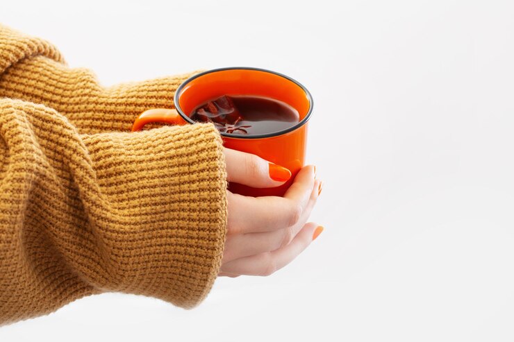 Foto mãos femininas com uma xícara de café laranja no fundo branco