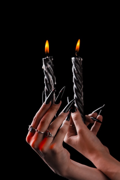 Mãos femininas com unhas compridas segurar velas acesas, bruxaria no dia das bruxas.