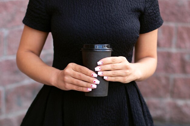 Mãos femininas com unhas de manicure da moda segurando uma xícara de café preta