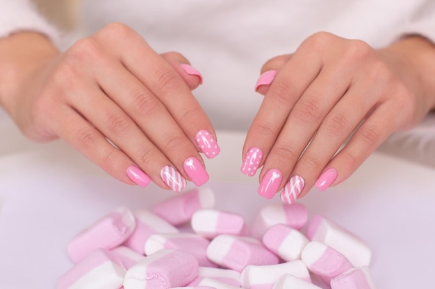 Mãos femininas com unhas de manicure rosa com marshmallow