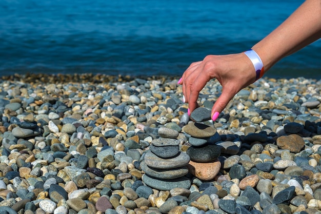 Mãos femininas constroem pirâmide de seixos equilibrada na praia contra o mar azul em dia ensolarado pedra cairn ao ar livre zen equilíbrio pedras meditação spa e conceito de harmonia