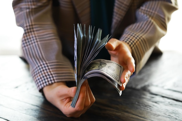 Mãos femininas contando notas de cem dólares americanos contra o fundo de notas menores de dinheiro sobre a mesa