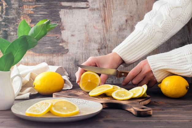 Mãos femininas cortam limões maduros em uma tábua de madeira e pedaços em um prato na mesa. Nutrição orgânica, fonte de vitaminas.