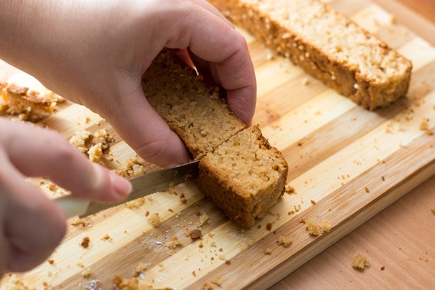 Mãos femininas cortando e preparando a crosta do bolo em um prato de madeira