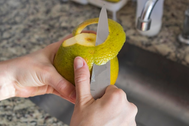 Mãos femininas cortando laranja na cozinha