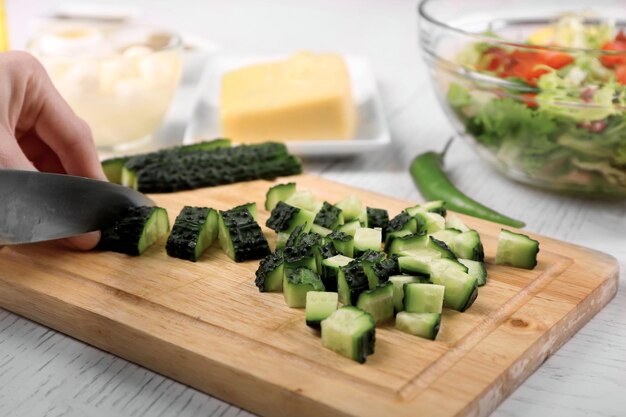 Mãos femininas cortando legumes para salada na cozinha