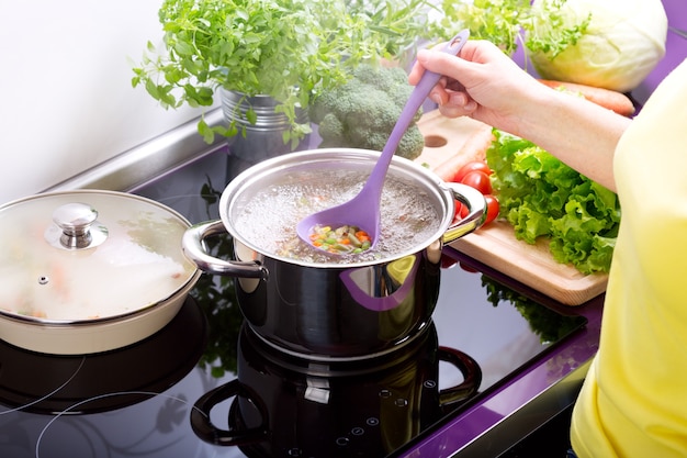 Mãos femininas cozinhando sopa de legumes na cozinha