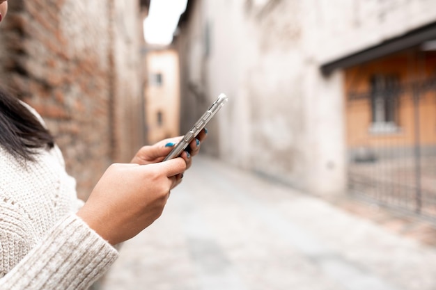 Mãos femininas de close-up segurando um smartphone. Mulher recortada irreconhecível usando telefone celular. Beco da cidade no fundo com espaço de cópia.