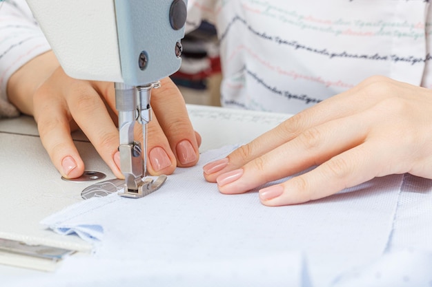 Mãos femininas de um alfaiate mestre no trabalho de uma agulha de máquina de costura