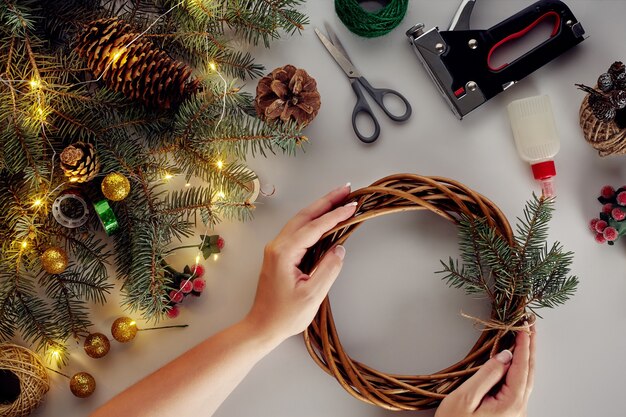 Mãos femininas decoram a guirlanda de Natal com ramos de abeto com uma fruta vermelha e cones da floresta. Fundo branco. Conceito de ano novo.