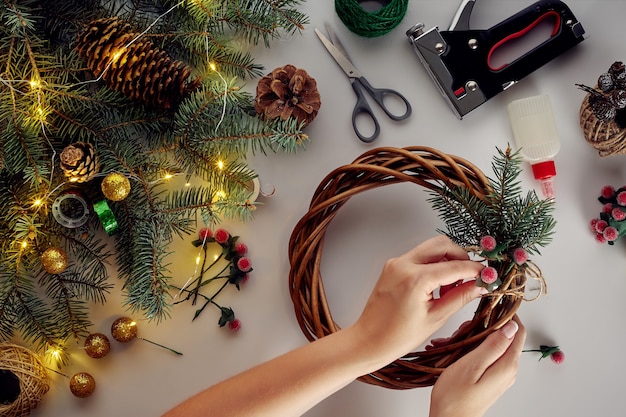 Mãos femininas decoram a guirlanda de Natal com ramos de abeto com uma fruta vermelha e cones da floresta. Fundo branco. Conceito de ano novo.