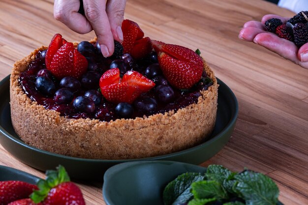 Foto mãos femininas decorando uma torta de bagas com frutas